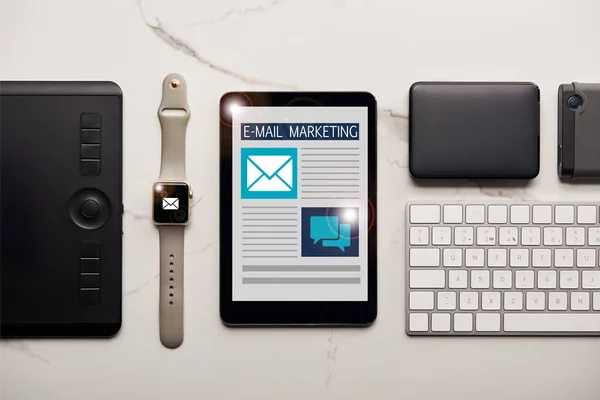 Disposición plana con varios dispositivos inalámbricos e ilustración de email marketing en la superficie de mármol blanco - foto de stock