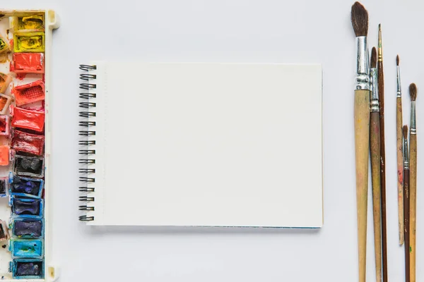 Draufsicht auf weißen Hintergrund mit Album zum Zeichnen, bunten Farben und Pinseln — Stockfoto