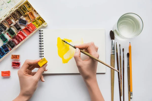 Top view of female hands drawing in album with watercolor paints and paintbrush — Stock Photo