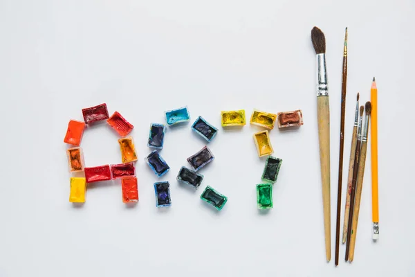 Vista superior de pinceles, lápices y letras de arte de pinturas sobre fondo blanco - foto de stock