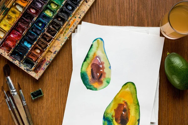 Top view of colored paints, paintbrushes and drawing with avocado on wooden background — Stock Photo