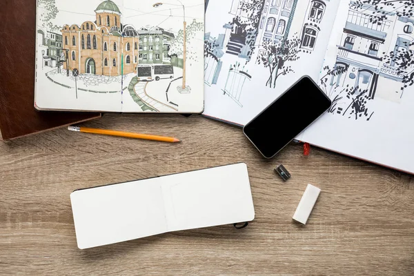 Vista dall'alto di immagini in album, utensili da disegno e smartphone su sfondo di legno — Foto stock