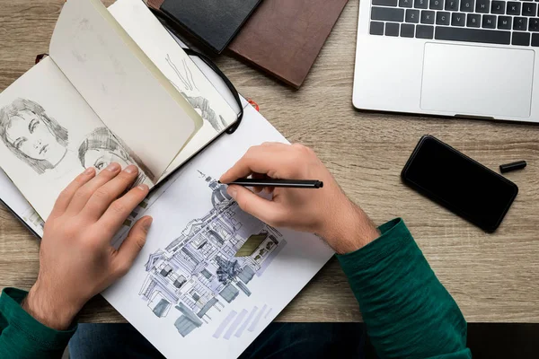 Vue du dessus des mains mans dessin dans l'album sur table en bois à côté du smartphone et ordinateur portable — Photo de stock