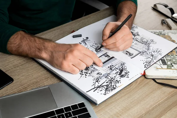 Foco seletivo de mãos de homem que desenha no álbum na mesa de madeira ao lado do computador portátil — Fotografia de Stock