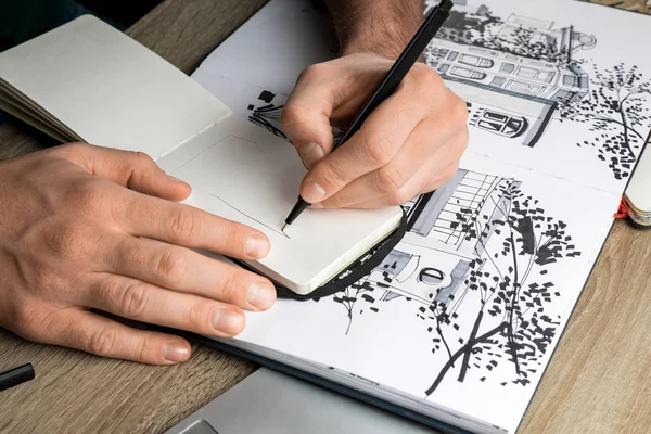 Selective focus of mans hands drawing in notebook on wooden table next to album — Stock Photo