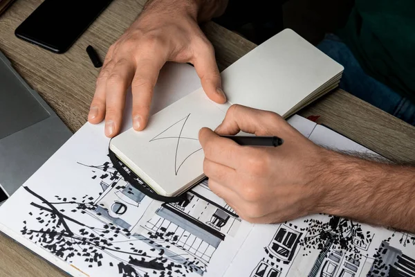 Enfoque selectivo de manos mans dibujo en cuaderno en mesa de madera al lado del álbum y gadgets - foto de stock