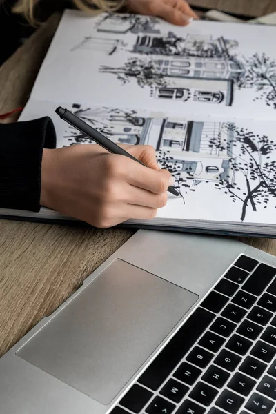 Selective focus of womans hands drawing in album on wooden table next to laptop — Stock Photo