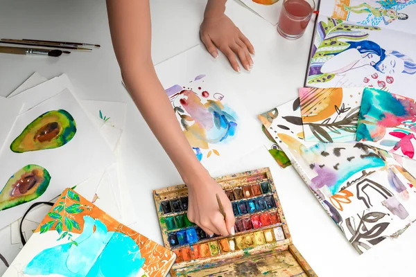 Fuoco selettivo di mani femminili che mescolano vernici ad acquerello circondate da immagini a colori — Foto stock