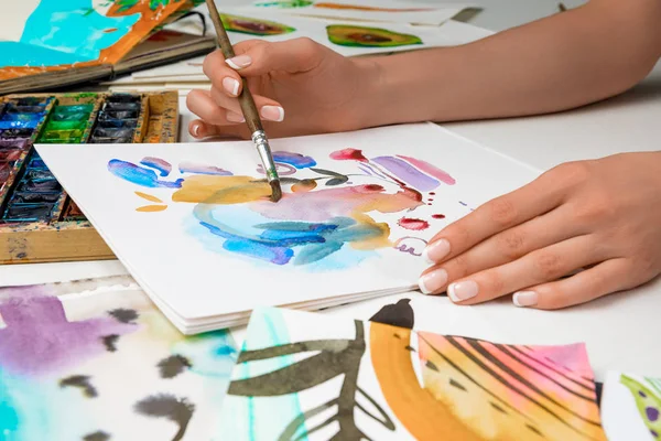 Selective focus of female hands drawing in album with watercolor paints and paintbrush — Stock Photo