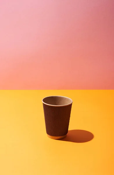 Taza de café de papel sobre la superficie amarilla y fondo rosa - foto de stock