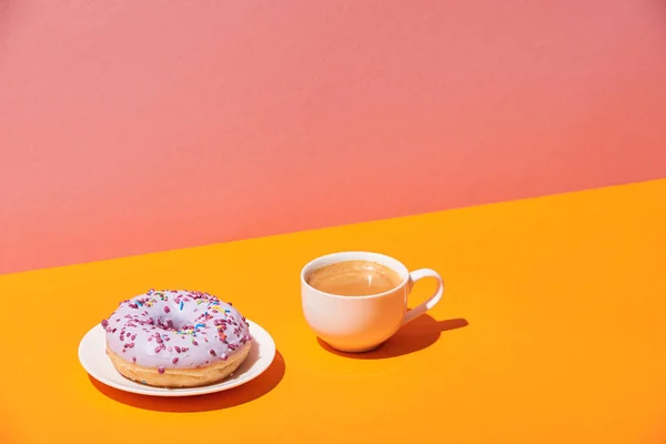 Leckerer Donut mit Untertasse und Kaffeetasse auf gelber Oberfläche und rosa Hintergrund — Stockfoto