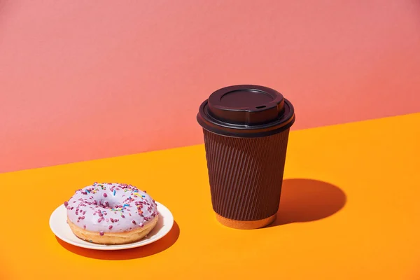 Sabroso donut con platillo y taza de café de papel sobre la superficie amarilla y fondo rosa - foto de stock