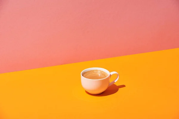 Coffee cup on yellow surface and pink background — Stock Photo