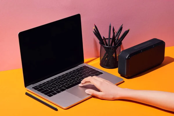 Обрезанный вид женщины с помощью ноутбука с чистым экраном рядом с держателем карандаша и динамиком — стоковое фото