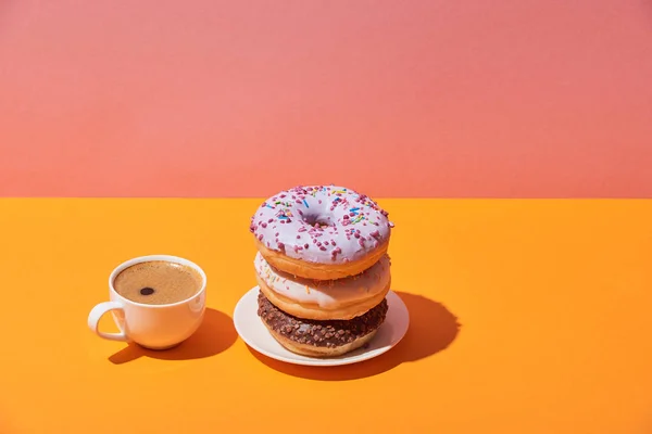 Saborosos donuts no pires e xícara de café na mesa amarela e fundo rosa — Fotografia de Stock