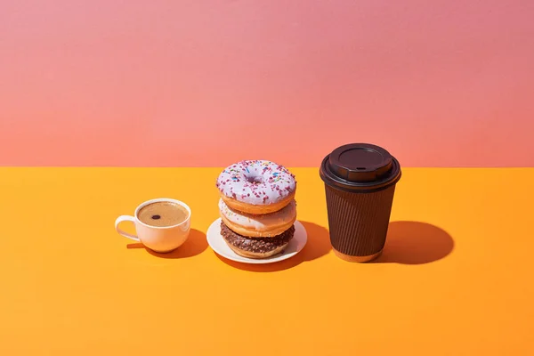 Sabrosos donuts en platillo y tazas de café sobre escritorio amarillo y fondo rosa — Stock Photo