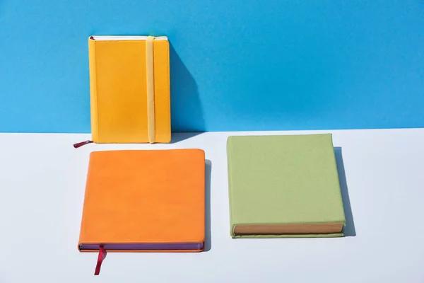 Cuadernos multicolores sobre escritorio blanco y fondo azul - foto de stock