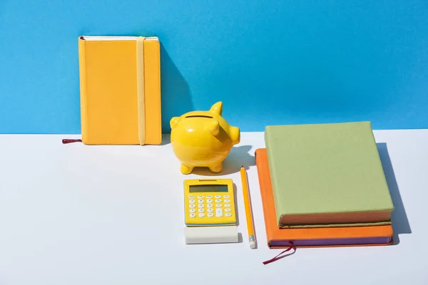 Notebooks multicoloridos, calculadora e porquinho banco na mesa branca e fundo azul — Fotografia de Stock