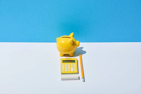 Calculadora, mealheiro, borracha e lápis na mesa branca e fundo azul — Fotografia de Stock