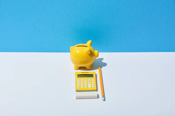 Calculator, piggy bank, eraser and pencil on white desk and blue background — Stock Photo