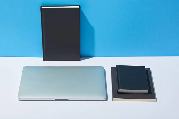 Laptop and notebooks on white desk and blue background — Stock Photo