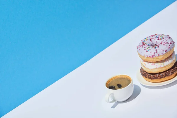 Saborosos donuts e xícara de café na mesa branca e fundo azul — Fotografia de Stock