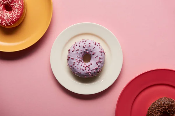 Vista superior de rosquillas dulces en platos sobre fondo rosa - foto de stock