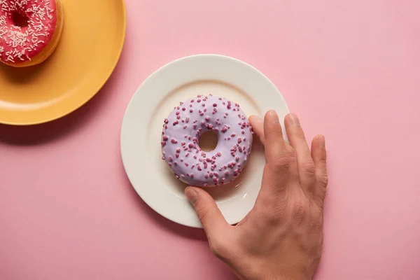 Vista ritagliata di uomo in possesso di ciambella smaltata in mano su sfondo rosa — Foto stock