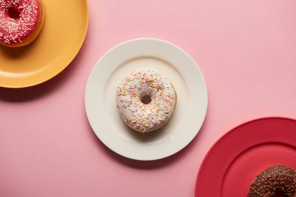 Vista superior de doces deliciosos donuts em pratos no fundo rosa — Fotografia de Stock