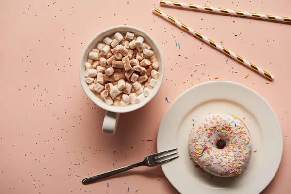 Вид сверху на сладкое какао с зефиром рядом с пончиком на розовом фоне — стоковое фото