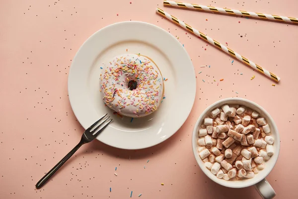 Vista superior de cacao dulce con malvaviscos cerca de donut sobre fondo rosa - foto de stock