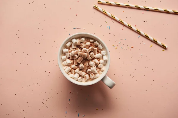 Vista superior de cacao dulce con malvaviscos cerca de bastones de caramelo sobre fondo rosa - foto de stock