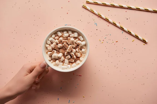 Vista recortada de la mujer sosteniendo taza de cacao en la mano sobre fondo rosa - foto de stock