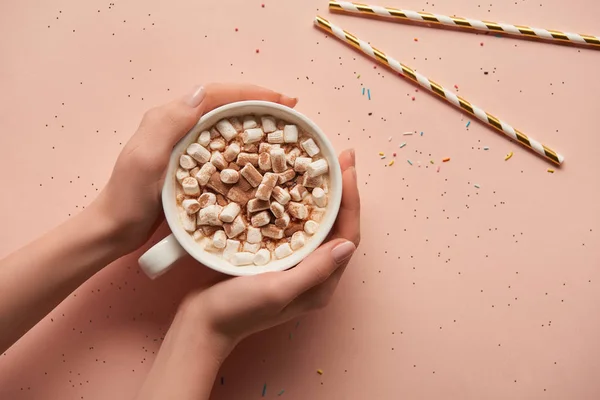 Cropped view of woman holding cup of cocoa in hands on pink background — Stock Photo