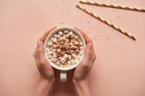 Vista recortada de la mujer sosteniendo taza de cacao caliente sobre fondo rosa - foto de stock