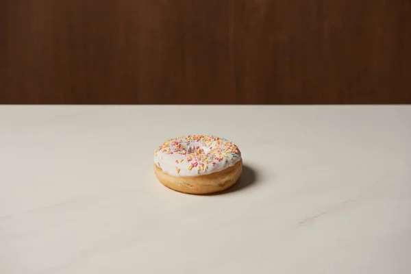 Sweet glazed donut with sprinkles on white table — Stock Photo