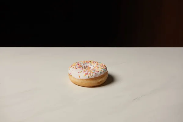 Sweet donut on white table isolated on black — Stock Photo