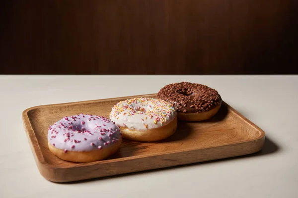 Tasty doughnuts with sprinkles on wooden cutting board — Stock Photo