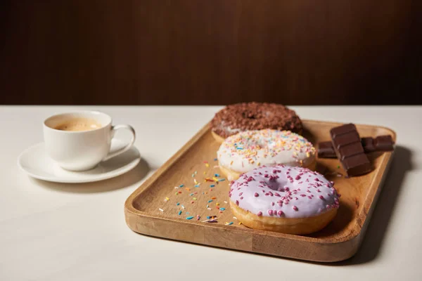 Glazed doughnuts with sprinkles on wooden cutting board near cup of coffee — Stock Photo