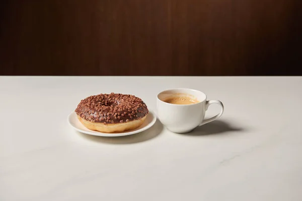 Glazed doughnut near cup of coffee on white table — Stock Photo