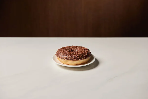 Glazed chocotale doughnut with sprinkles on white table — Stock Photo