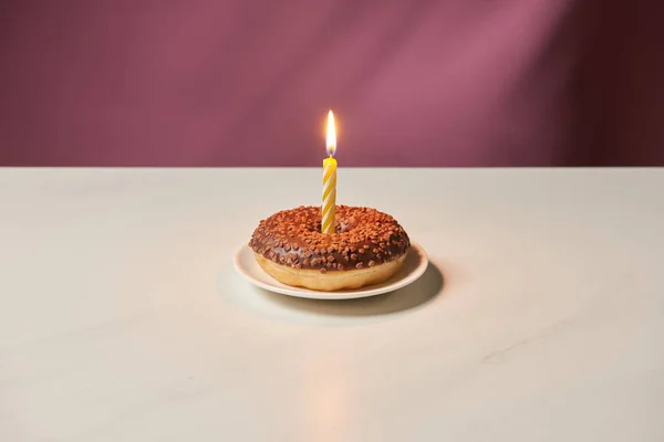 Burning candle in middle of doughnut with icing and sprinkles on white table — Stock Photo