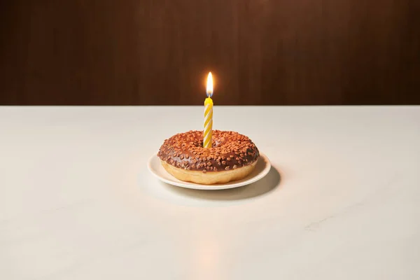Burning candle in middle of sweet doughnut with icing and sprinkles on white table — Stock Photo