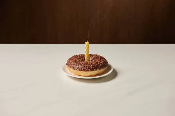 Bougie au milieu du beignet avec glaçage et saupoudrer sur table blanche — Photo de stock