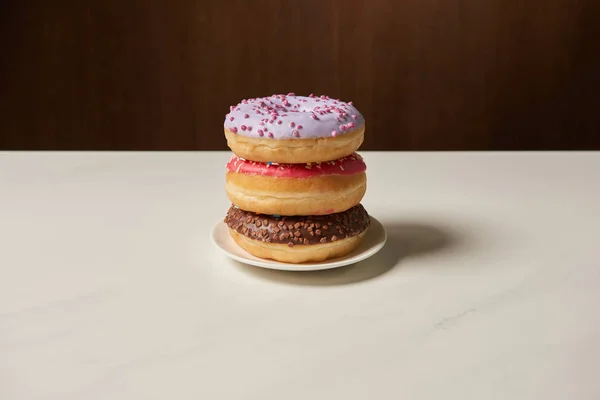 Leckere Donuts mit Zuckerguss und Streusel auf Teller auf weißem Tisch — Stockfoto