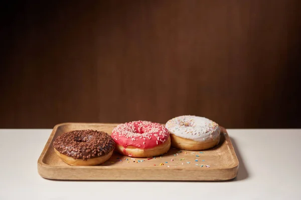 Leckere Donuts mit Zuckerguss und Streusel auf Holzschneidebrett — Stockfoto