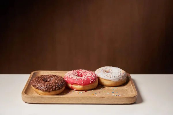 Sabrosas rosquillas con glaseado y espolvoreado sobre tabla de cortar de madera - foto de stock