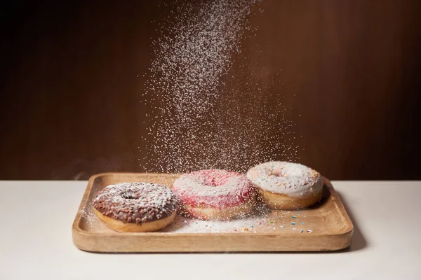 Tasty donuts with sifting sugar powder on wooden cutting board — Stock Photo