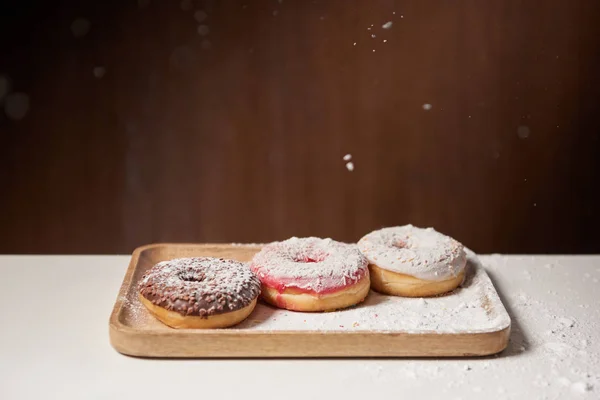 Saborosos donuts com açúcar em pó na placa de corte de madeira — Fotografia de Stock