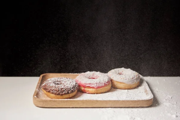 Delicious donuts with sifting sugar powder on wooden cutting board — Stock Photo